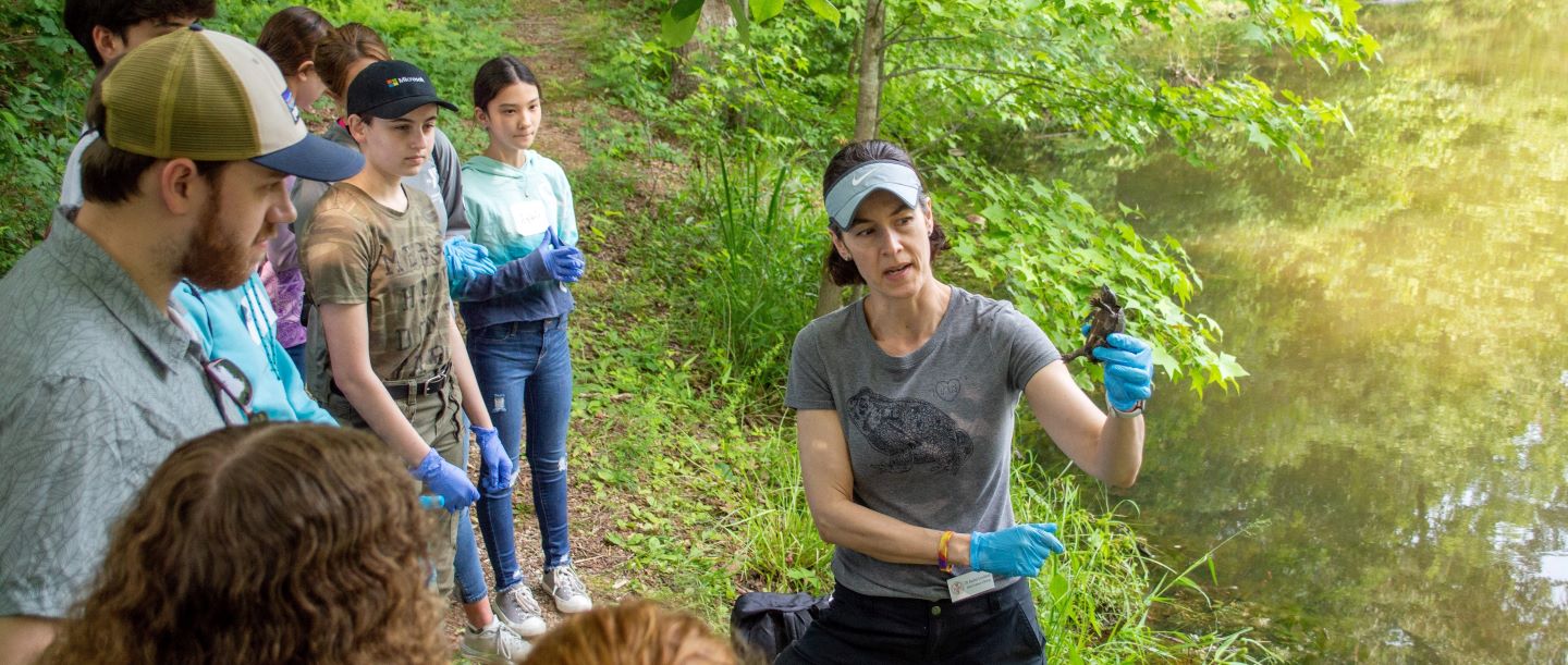 Biology professor showing student a turtle at the edge of a pond