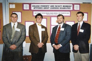 Three students and their professor standing in fornt of their poster presentation