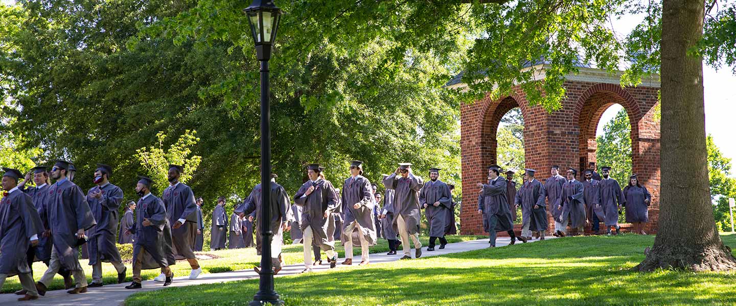 students in regalia process through the Bell Tower 