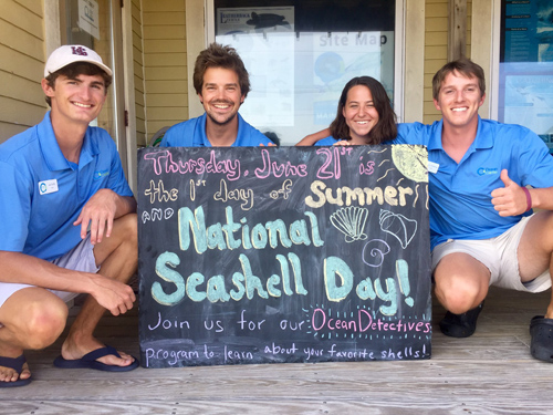 Four interns pose with a sign advertising National Seashell Day