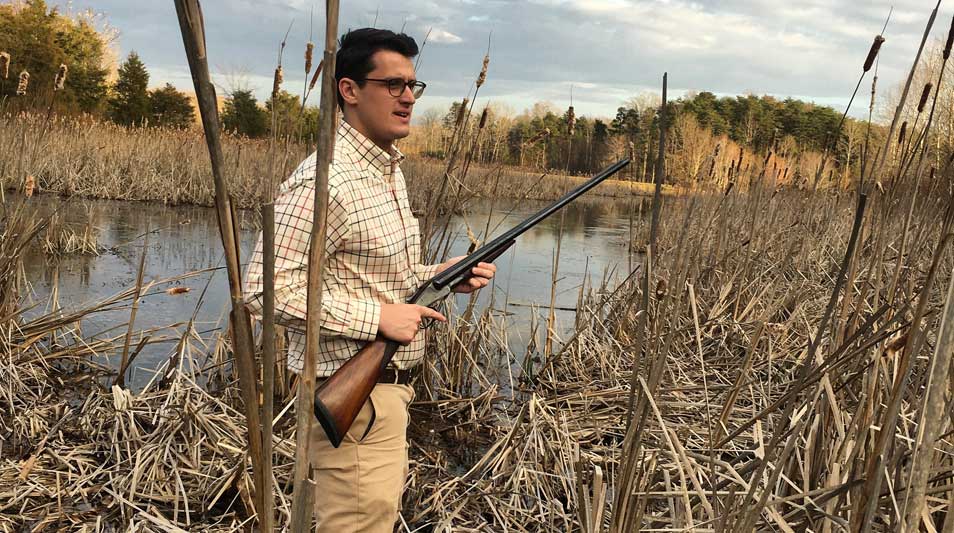 Phillip Beatty ‘18, co-founder of Randolph & Overstreet, showcases a 1902 L.C. Smith shotgun standing on the edge of a lake.
