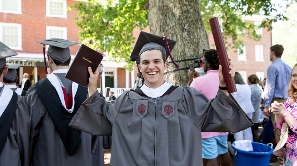 A graduate smiles with his diploma and bible.