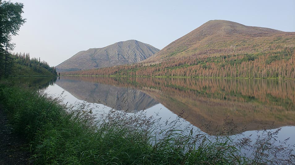An Alaskan lake mirrors the image of a mountain nearby