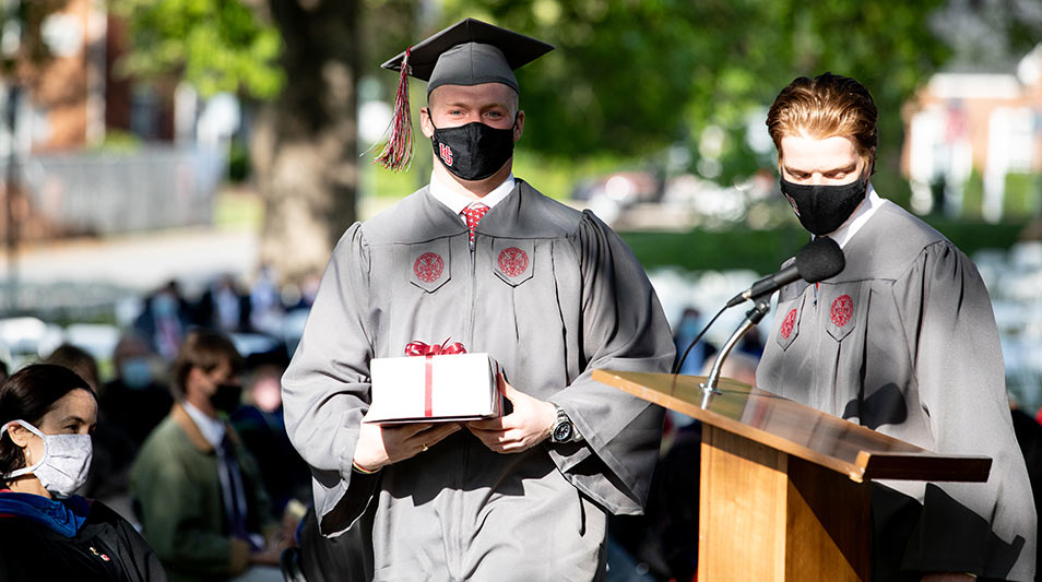 Hampden-Sydney student in regalia holdin an award at the podium