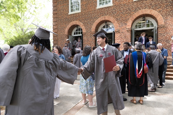 The class of 2025 in regalia shaking hands outside the auditorium