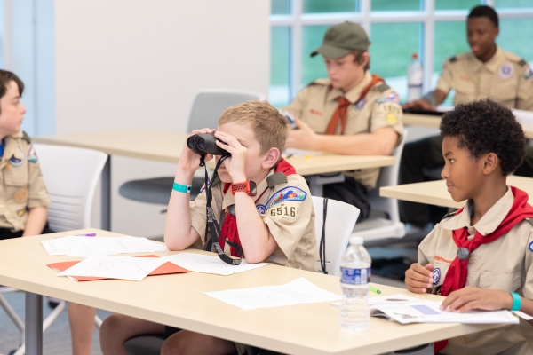 a scout in uniform peers through binoculars