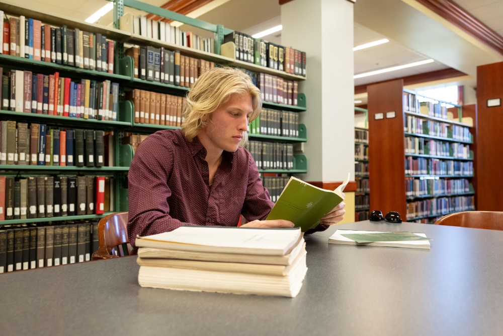 Bryson Smith reading a book in the Bortz Library stacks