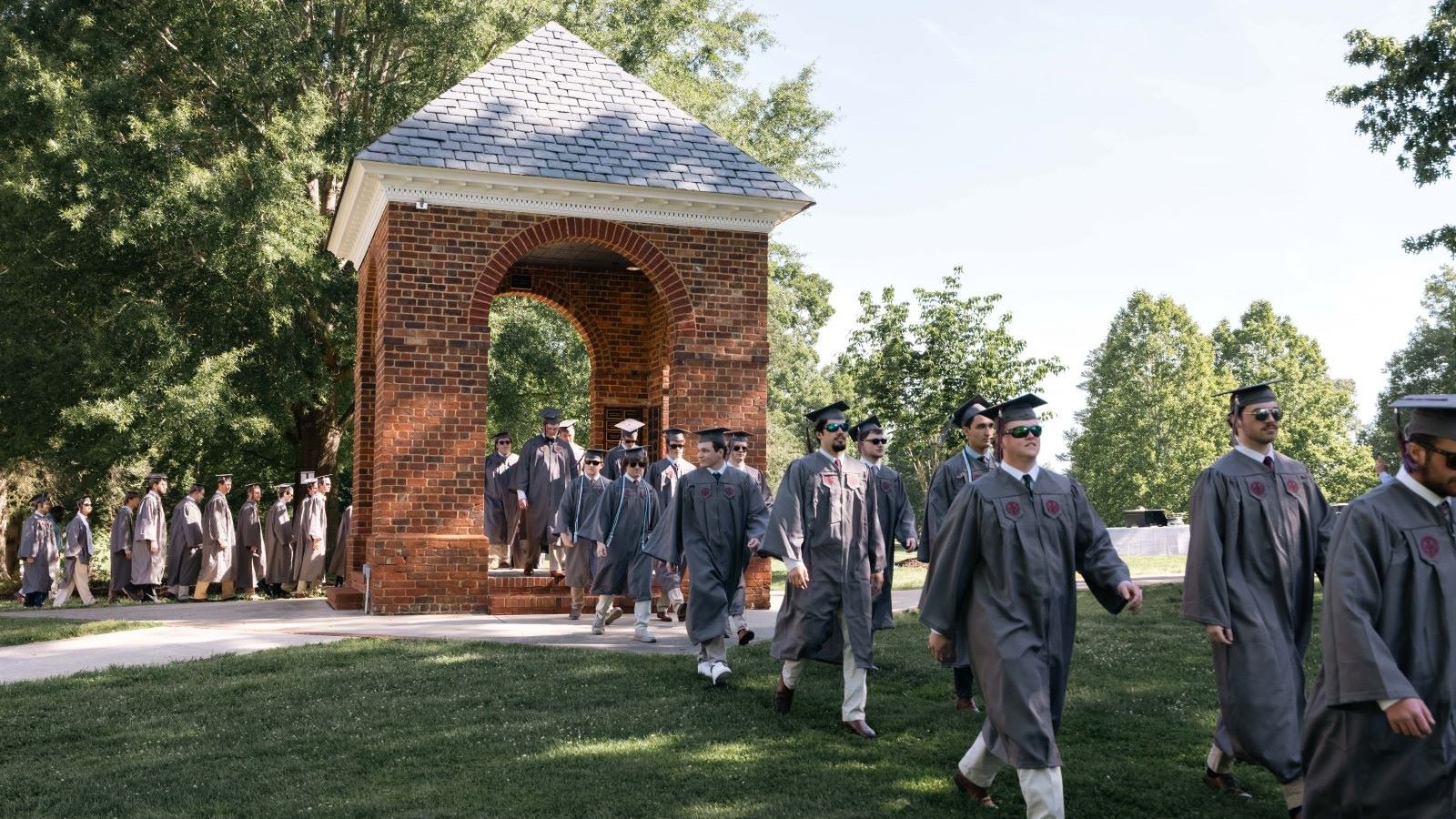Graduating students in regalia walking through the Bell Tower at Hampden-Sydney College