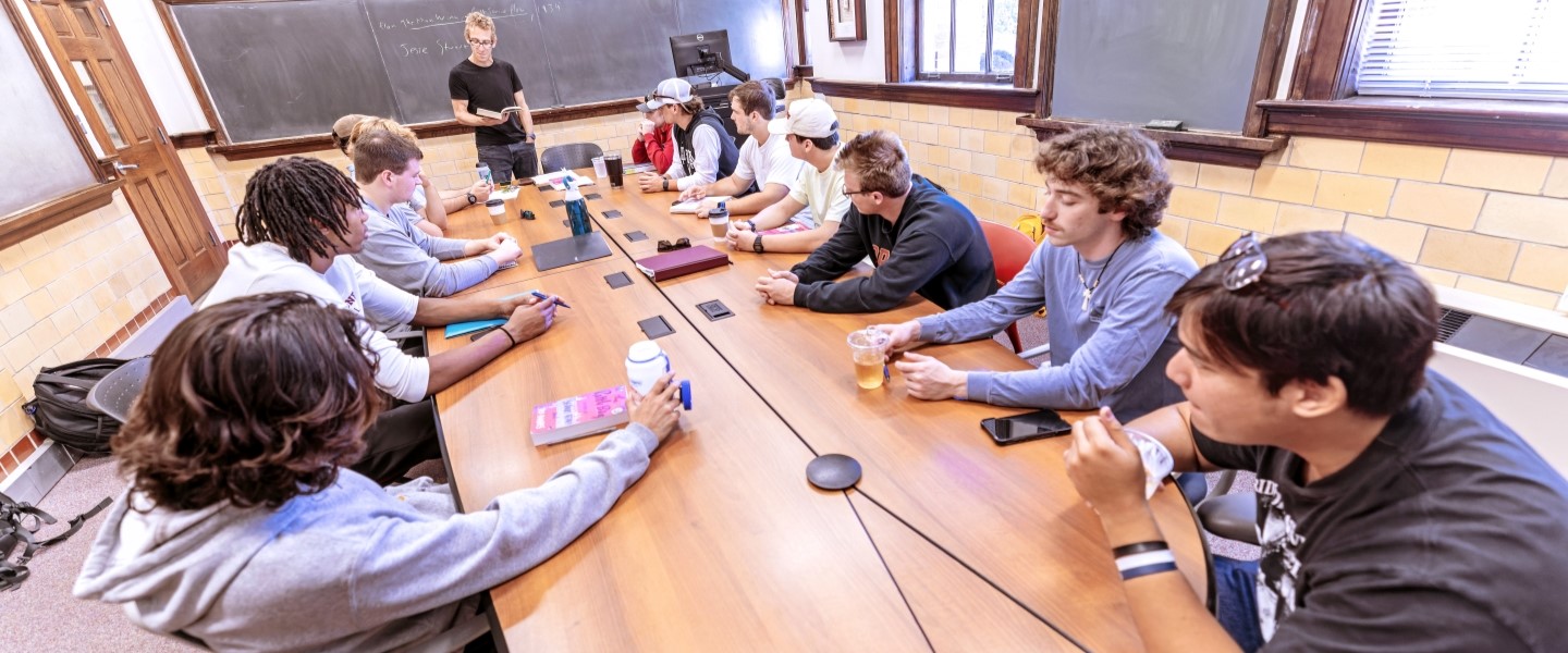 students sitting in a traditional classroom led by a professor at a blackboard