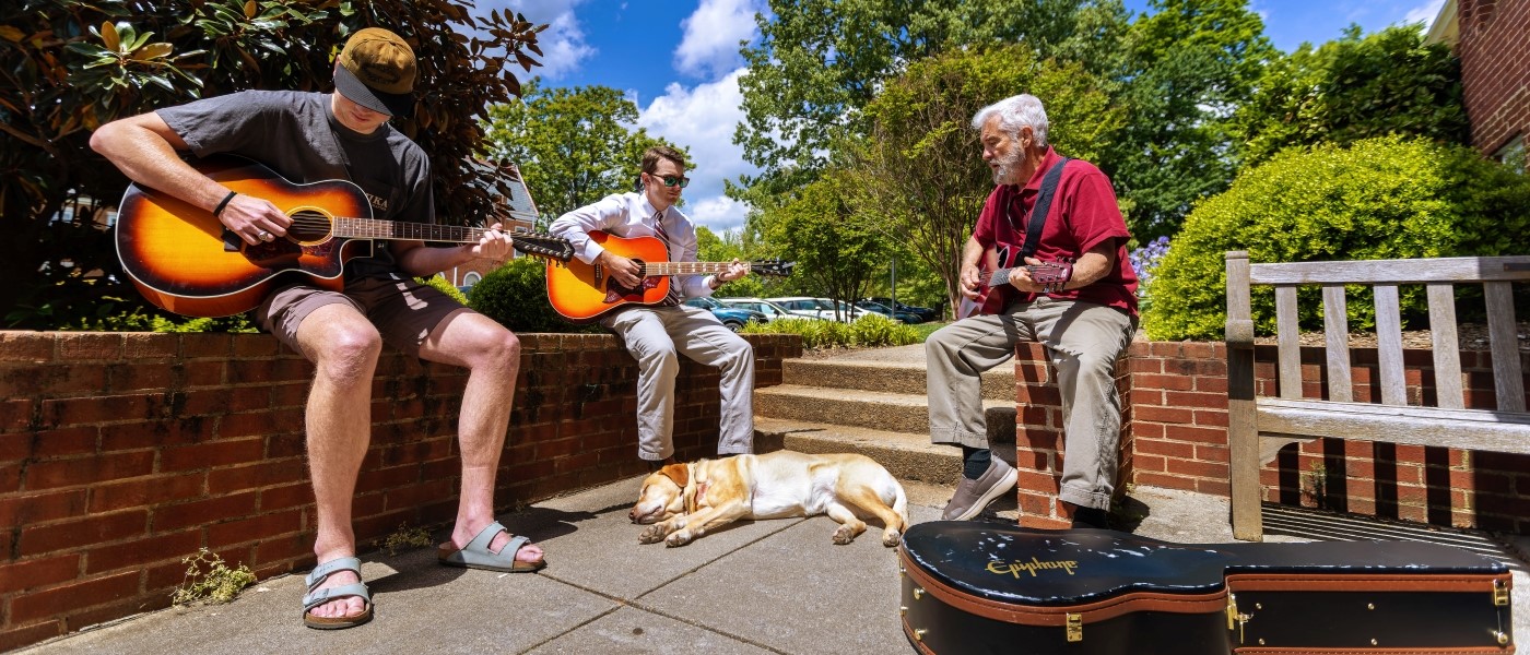 students sitting outdoors learning guitar skills form an instructor 