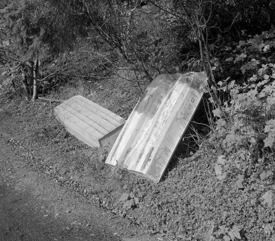 black and white image of a skiff sitting on a dirt road: by Patrice Aphrodite Helmar, "Two Skiffs," 2018