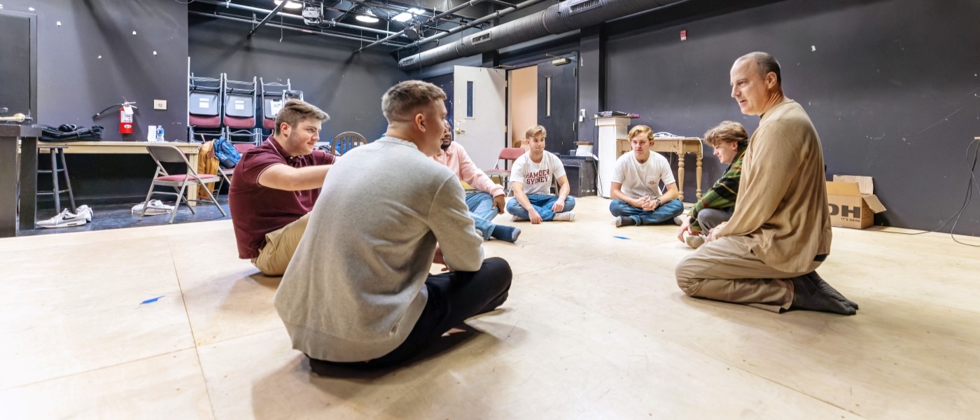 Professor and students sitting in a circle on a stage