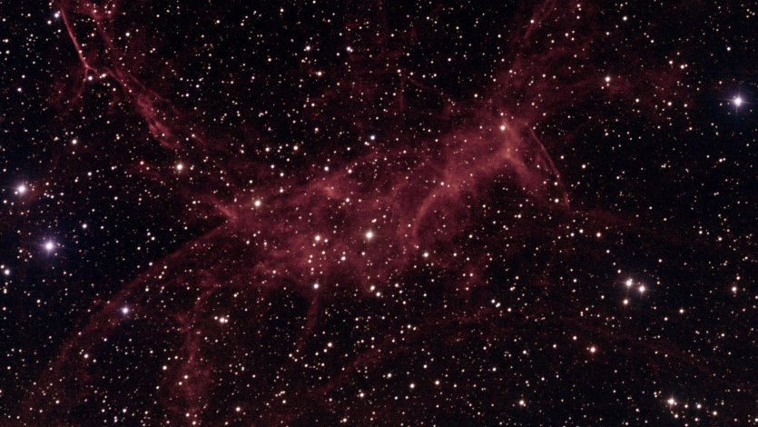deep image of the Spaghetti Nebula (Simeis 147 / Sh2-240), showing faint red hydrogen filaments from an ancient supernova remnant spread across a dense star field