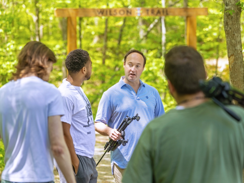 a professor and students meeting by a trail