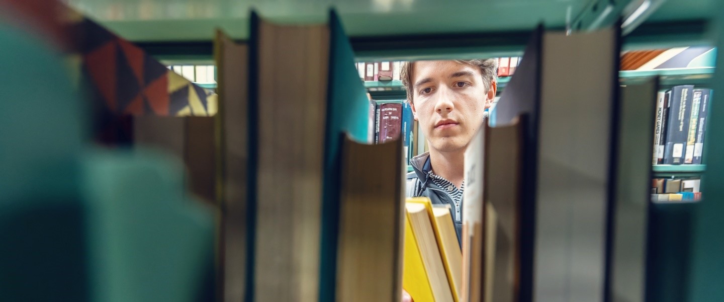 a student looking through a stack of library books at Hampden-Sydney.