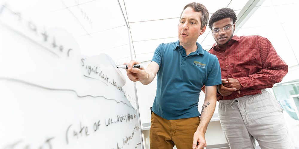 a professor working with his student at the board in the rhetoric studio