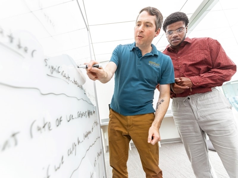professor writing a sentence with a student on the whiteboard