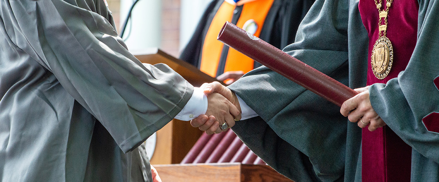 a close-up image of a graduate receiving his degree and shaking hands with the College president