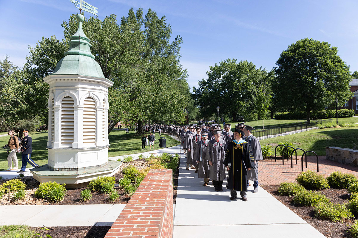 Class of 2025 in regalia processing along the sidewalk