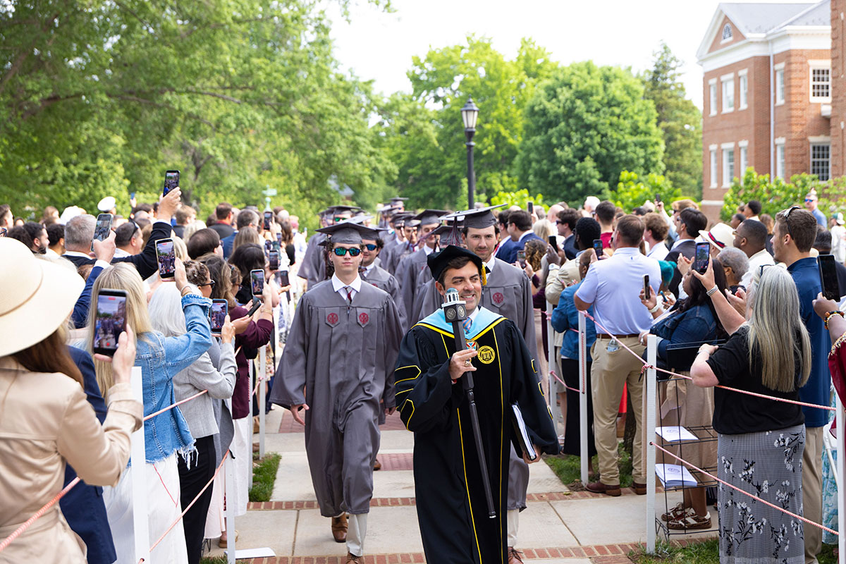 Class of 2026 led by the Dean of Students in regalia processing to the commencement ceremony