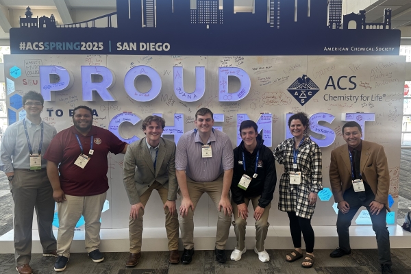 students and professor pose in a group at a conference