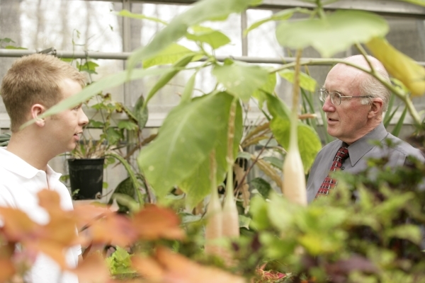 Dr. Shear standing in a greenhouse with a student