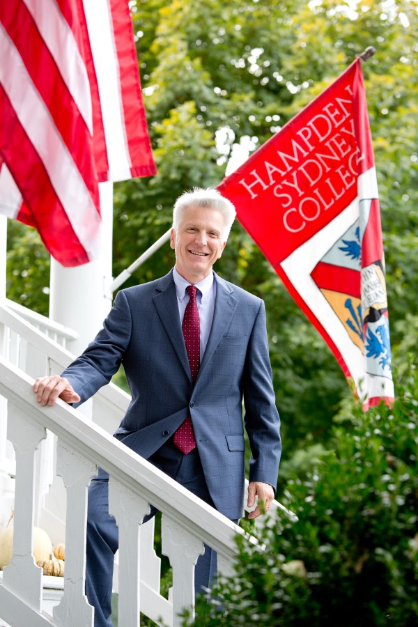 President Stimpert standing on the porch in front of the Hampden-Sydney flag