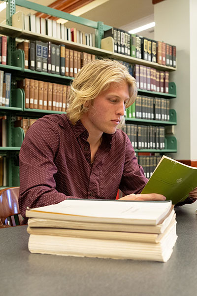 Bryson Smith reading a book in the Bortz Library stacks