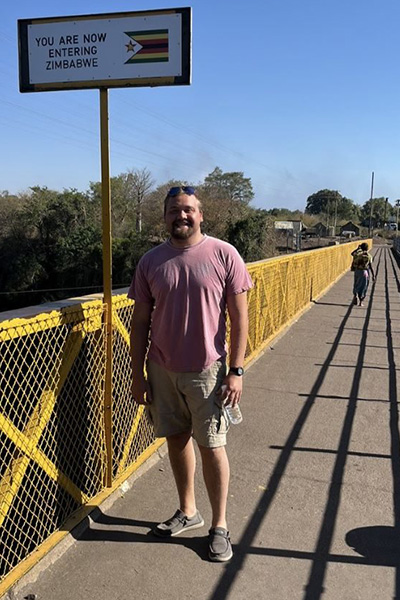Carter Spawn on a bridge in front of a sign that says, "Zimbabwe"