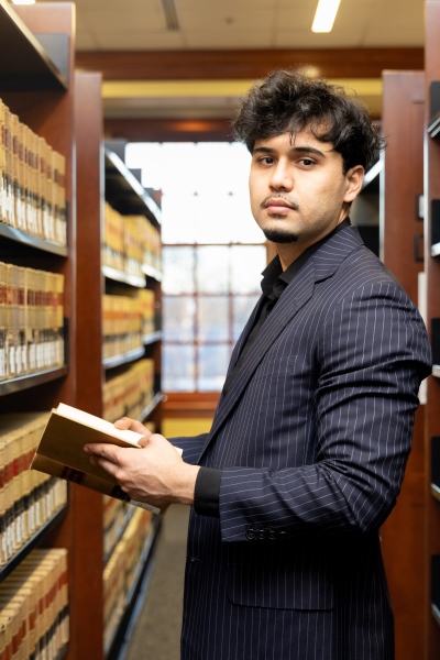 Kamal Iqbal '27 standing in the the library stacks with a book