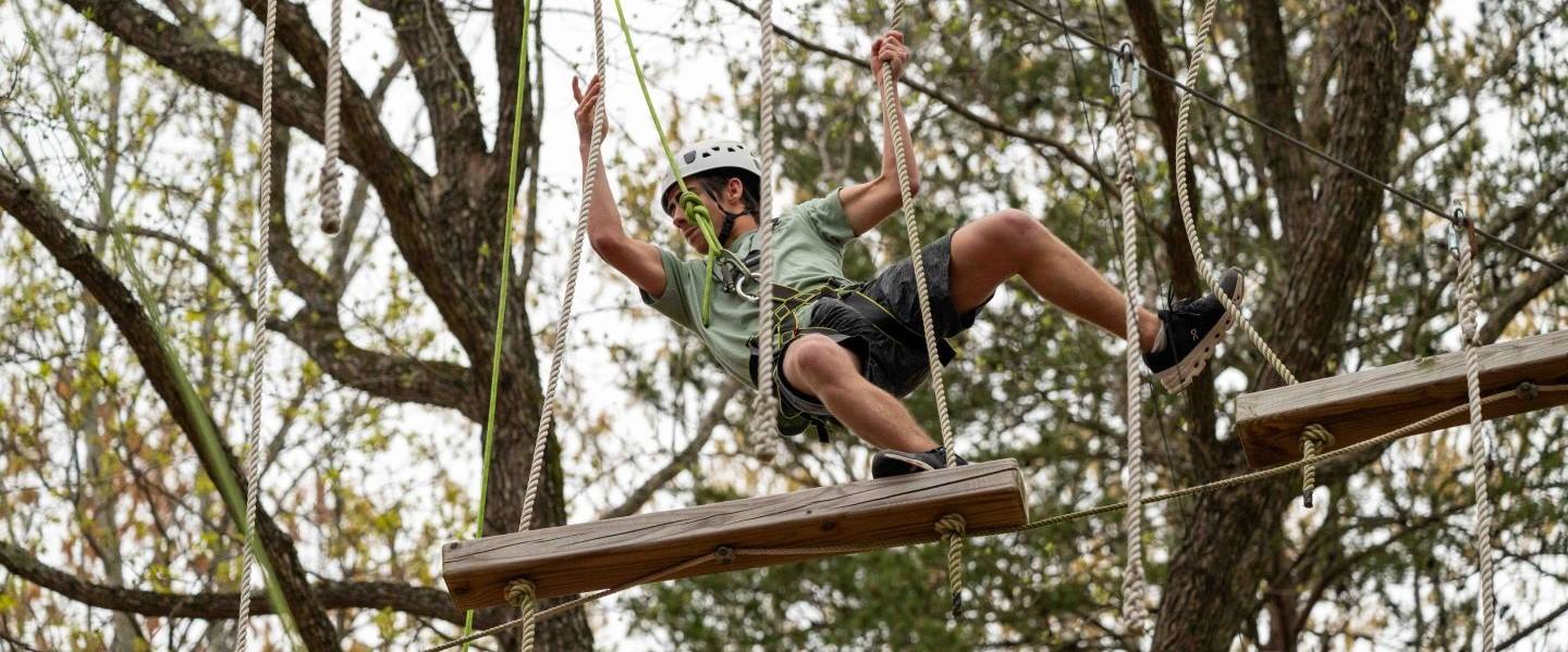 a student traversing a rope in the trees on Hampden-Sydneys's high rope course