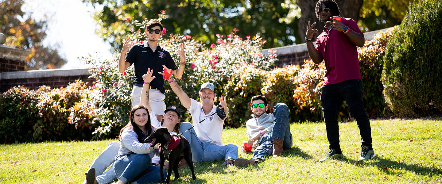Friends sitting in the grass at a football game at Hampden-Sydney College