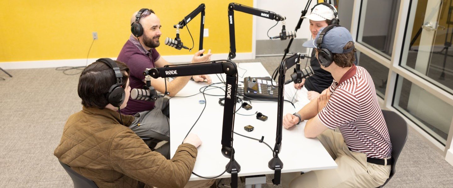 Students sitting around microphones recording a podcast
