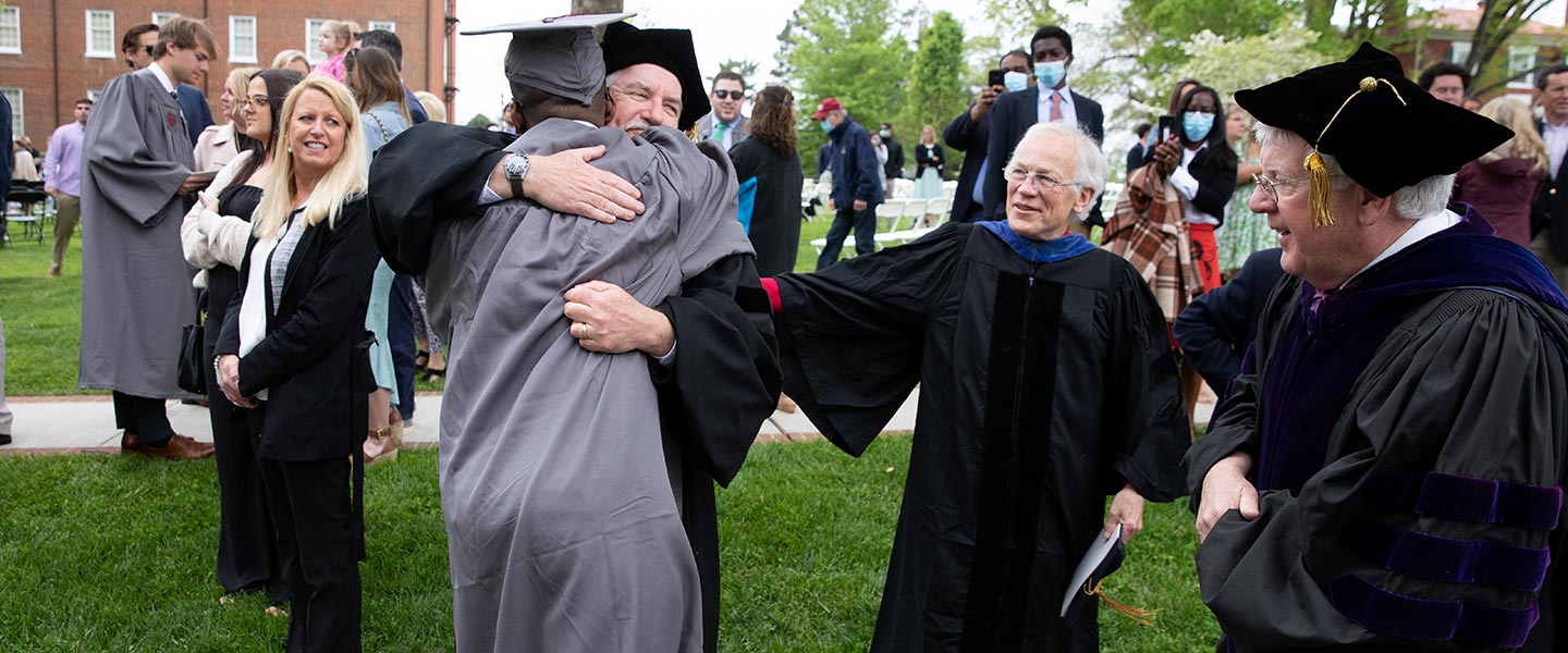Faculty members hugging a graduate commencement at Hampden-Sydney College