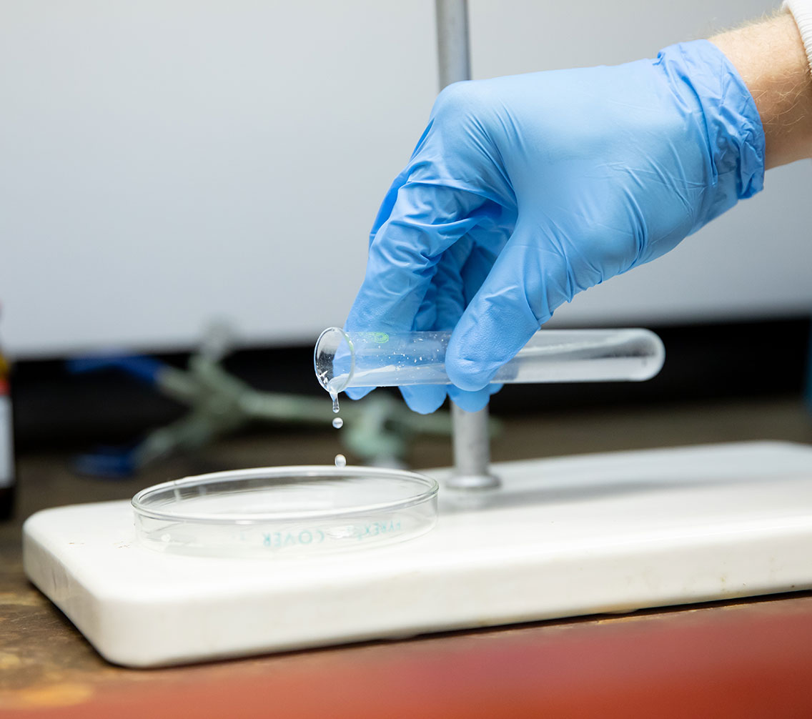 Close-up laboratory photo of a gloved hand pouring from a beaker