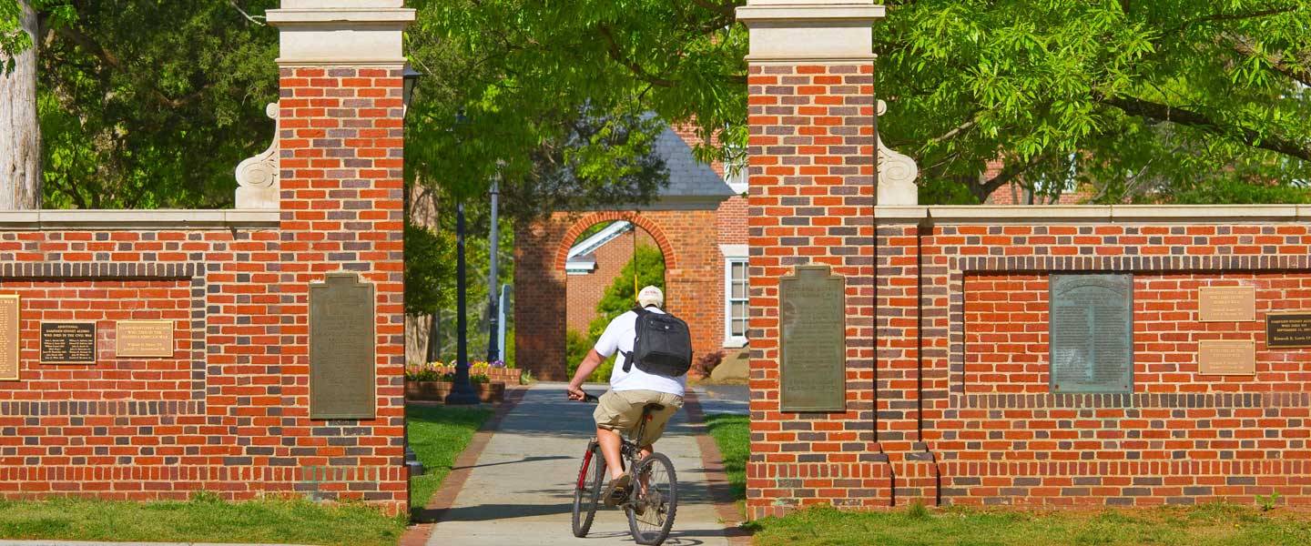 Student biking through memorial gates at Hampden-Sydney College