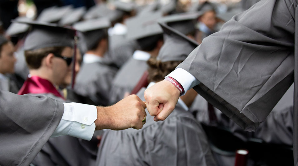 two college graduates  in regalia fist bumping
