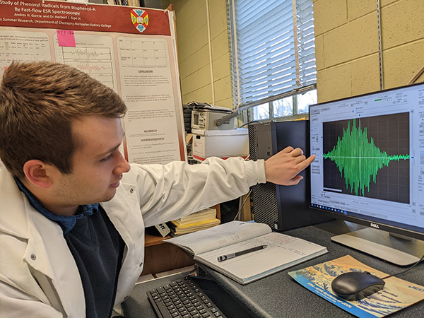 A studentin a labcoat pointing to a graph on the computer screen