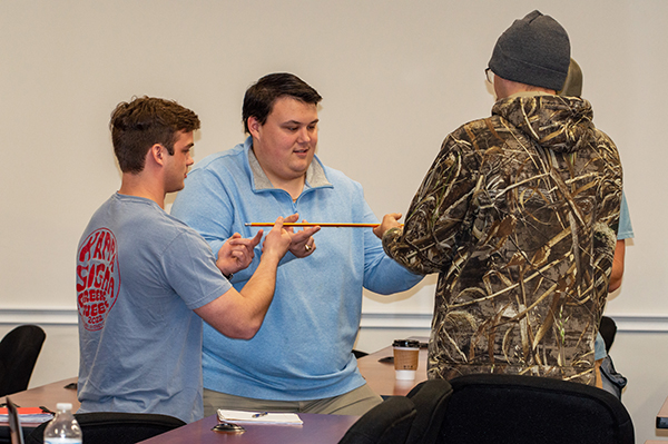 Students cooperating to balance a metal rod on their fingers
