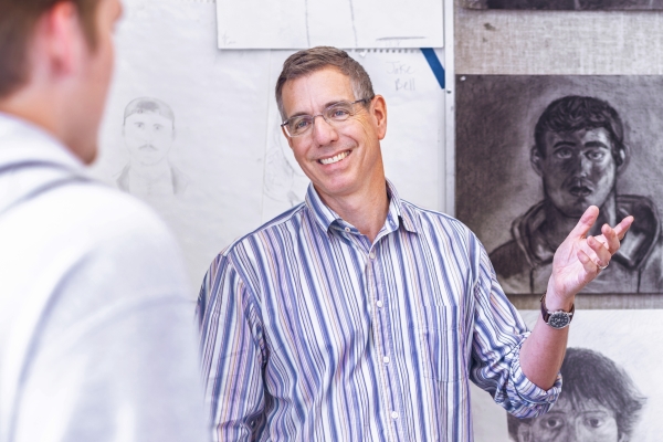 Ray Kleinlein standing in a gallery with his students and their artwork