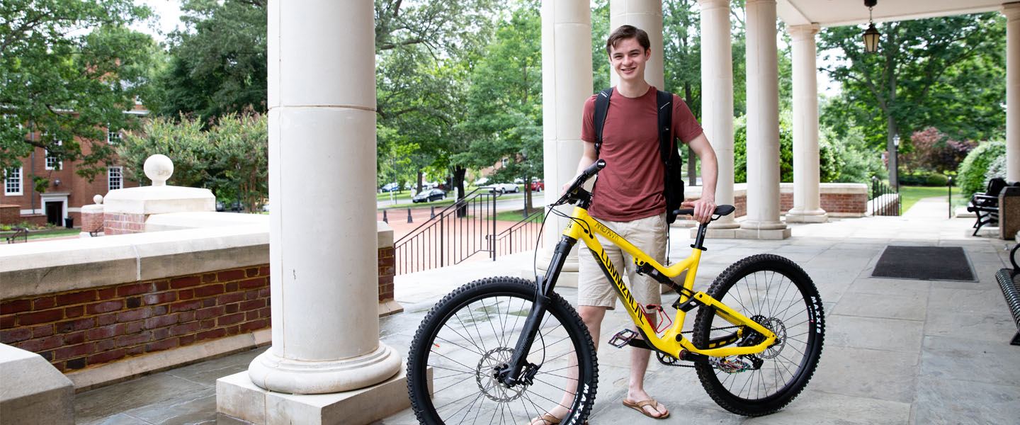 David Fluharty '20 with a bike in front of Bortz Library.