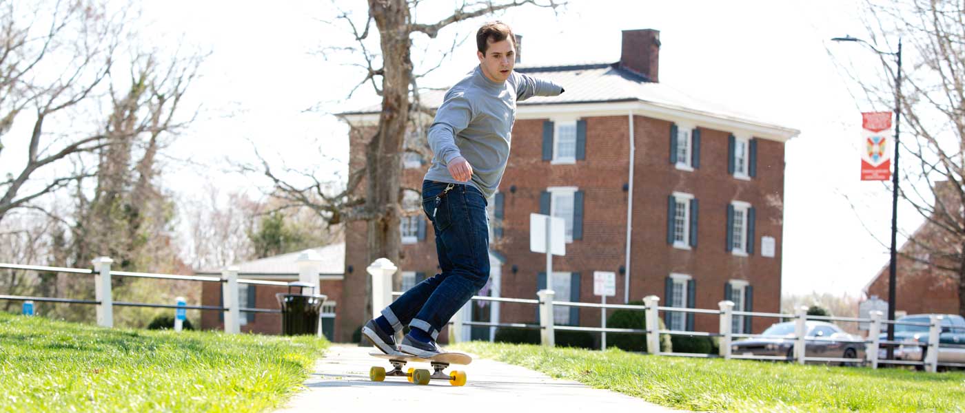 Sam Murphy '18 skateboarding along a sidewalk at Hampden-Sydney College.