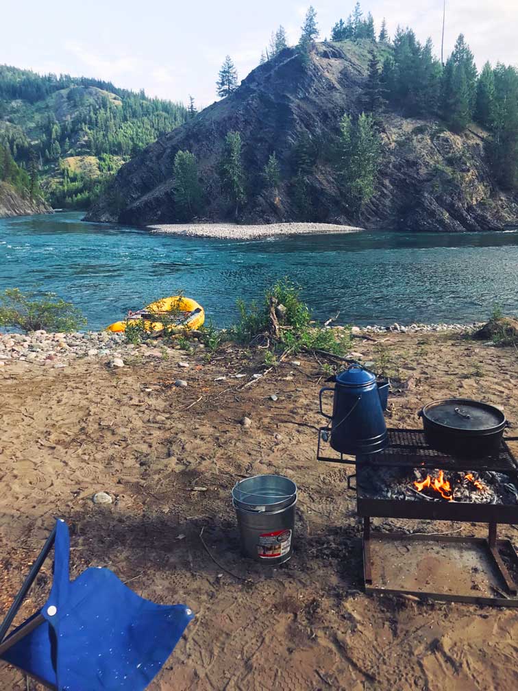 A campsite with a fire pit sits on the banks of the river in Glacier National Park
