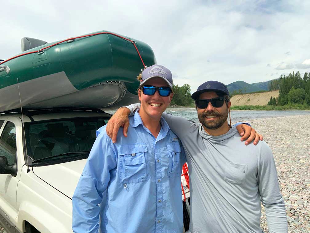 Sam McLean and Nate Tubner stand in front of a car with a boat on top of it.