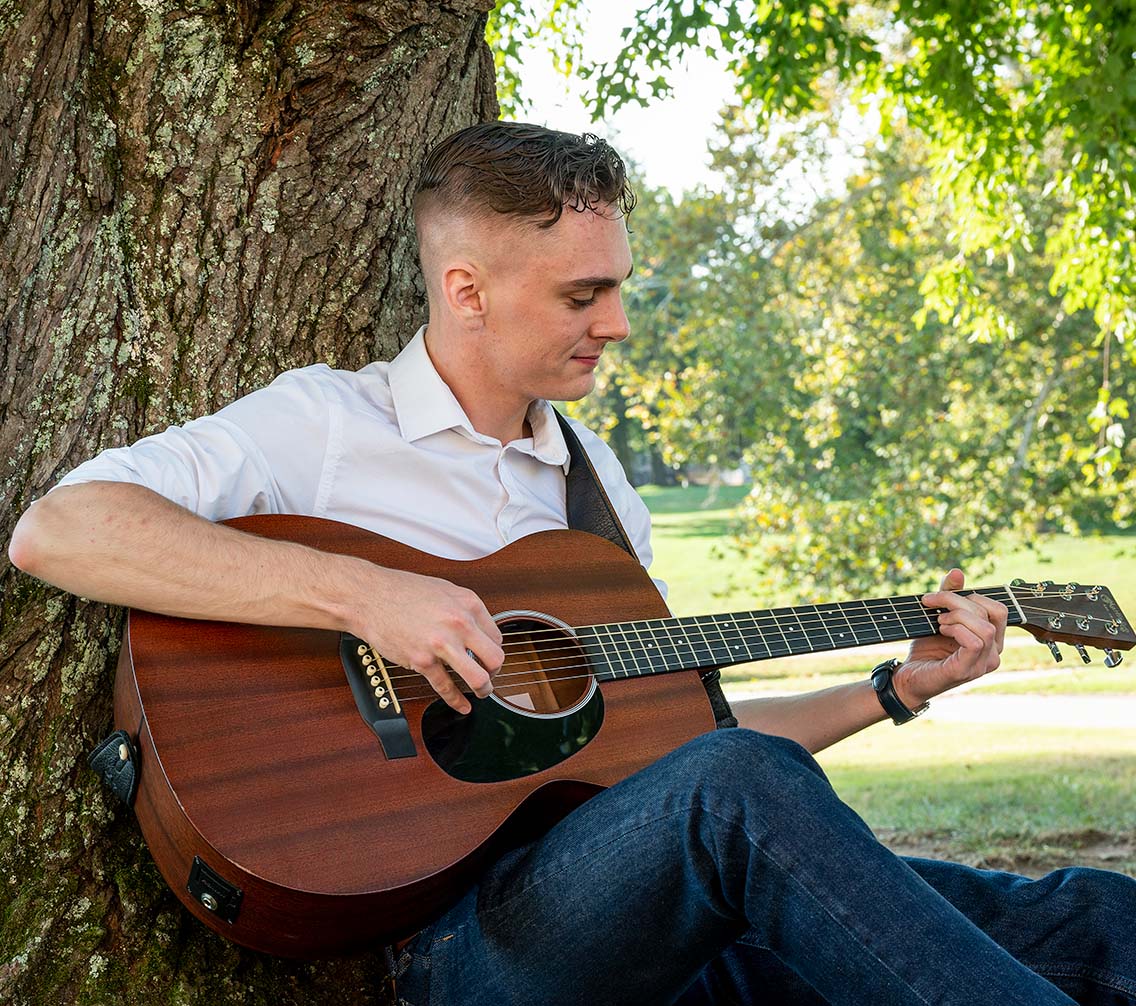 Ben Hager '23 strumming a guitar under a tree