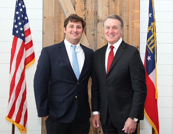 Cal Mitchell with Senator Perdue between two flags