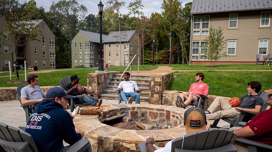A view of The Grove residence hall and students sitting at a  firepit
