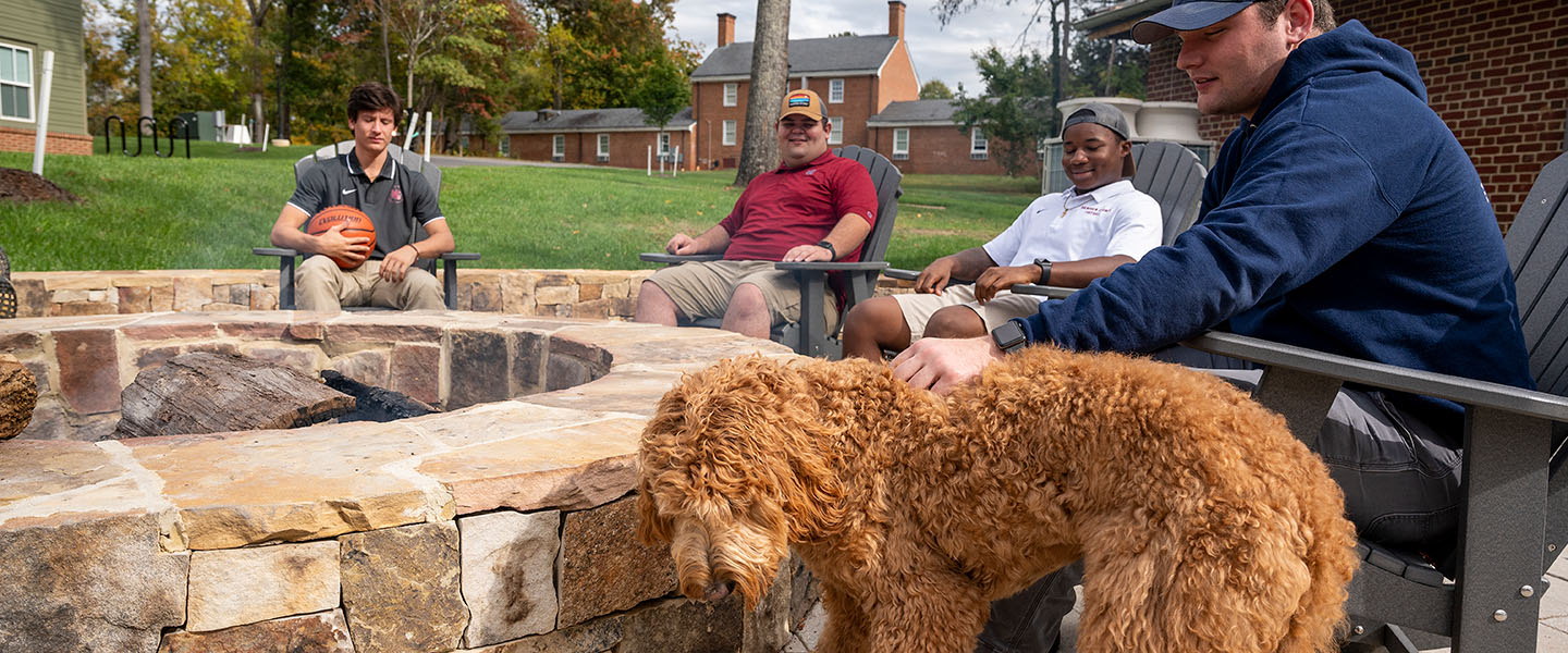 Hampden-Sydney College students and a dog sitting around a firepit